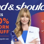 Head & Shoulders ad featuring a smiling woman in a white coat holding a blue shampoo bottle; headline claims up to 100% elimination of stubborn dandruff with visible flakes noted below, and a large orange circular graphic on the right.